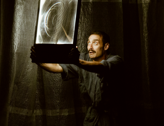 Thumbnail of http://A%20man%20gazes%20upwards,%20holding%20a%20glowing,%20swirling%20light%20box.%20He%20stands%20against%20a%20dark,%20textured%20curtain,%20creating%20a%20dramatic%20and%20mysterious%20atmosphere.