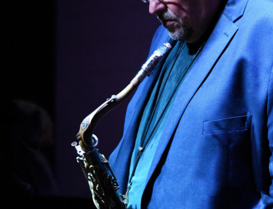 Thumbnail of http://Man%20in%20a%20blue%20blazer%20playing%20a%20saxophone%20under%20soft%20lighting,%20focused%20and%20introspective.%20The%20atmosphere%20feels%20calm%20and%20intimate.
