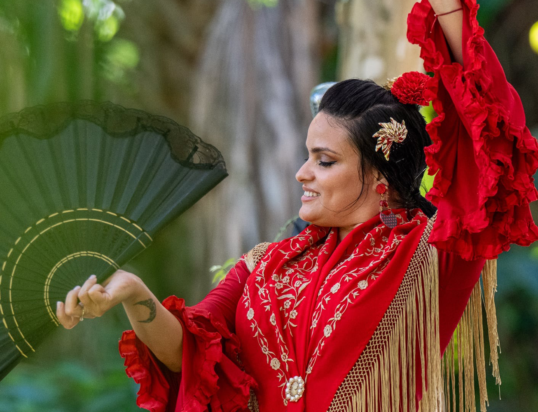 Thumbnail of http://A%20woman%20in%20a%20vibrant%20red%20flamenco%20dress%20holds%20a%20black%20fan,%20gracefully%20dancing.%20Her%20expression%20is%20joyful,%20surrounded%20by%20lush%20greenery,%20conveying%20elegance.