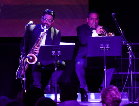 Thumbnail of http://Two%20men%20in%20suits%20performing%20on%20stage,%20one%20playing%20a%20saxophone%20and%20the%20other%20playing%20a%20trumpet,%20creating%20a%20lively%20musical%20atmosphere%20before%20an%20audience.